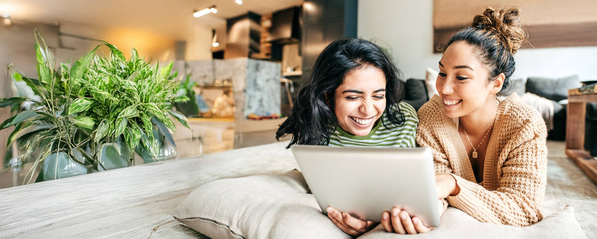 Zwei Frauen lächeln während sie auf das Tablet schauen.