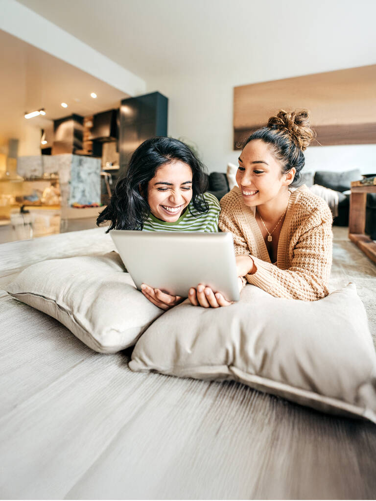 Zwei Frauen lächeln während sie auf das Tablet schauen.
